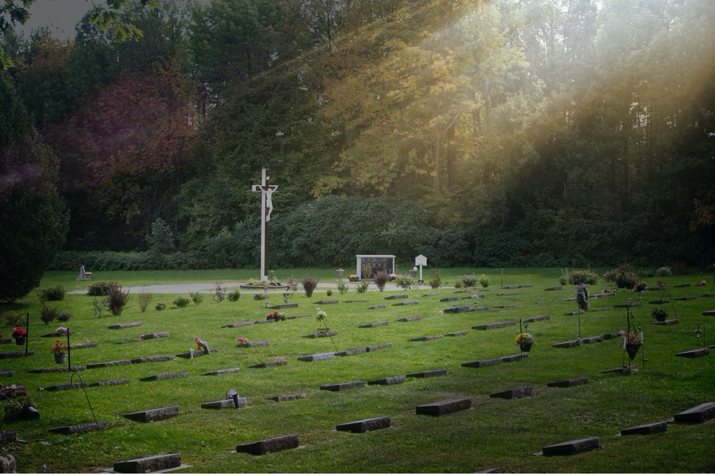 St. Margaret's Cemetery in the summer with the sun beaming down onto a large crucifix and many graves.