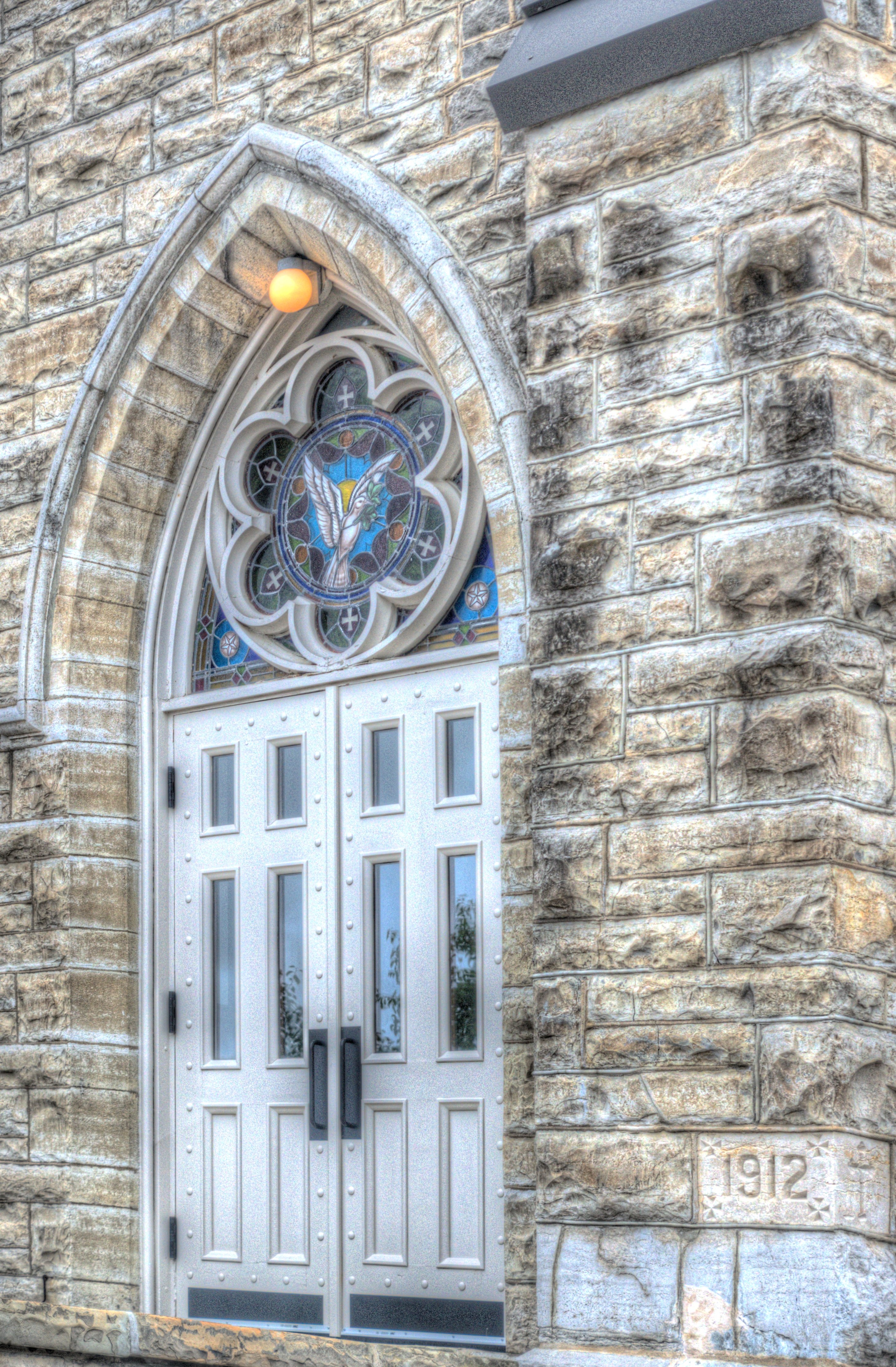 Outside image of St. Margaret's beautiful front doors with a holy spirit dove stain glass above the door.