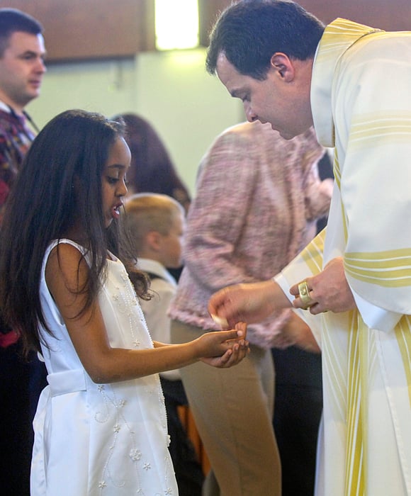 A priest leaning down giving First Communion to a young girl.